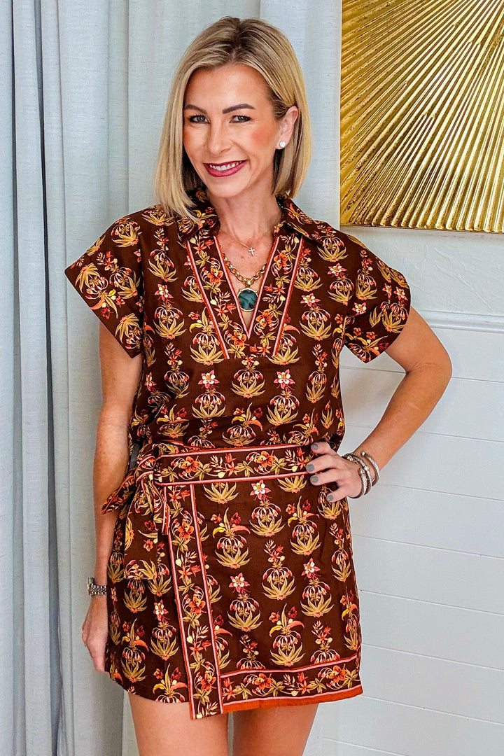 Woman wearing the Autumn Garden Border Print Skort Set, a brown floral two-piece with a short sleeve V-neck top and wrap-front skort