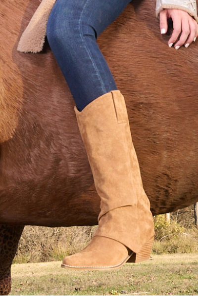 Camel suede knee-high western boot with pointed toe, stacked heel, and subtle western seam detailing, styled with dark denim.